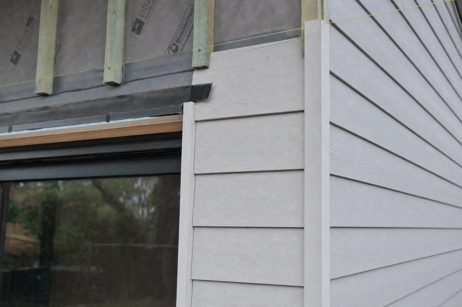 Fibre cement cladding set out around a window opening with head flashing, timber reveal and corner trim in place