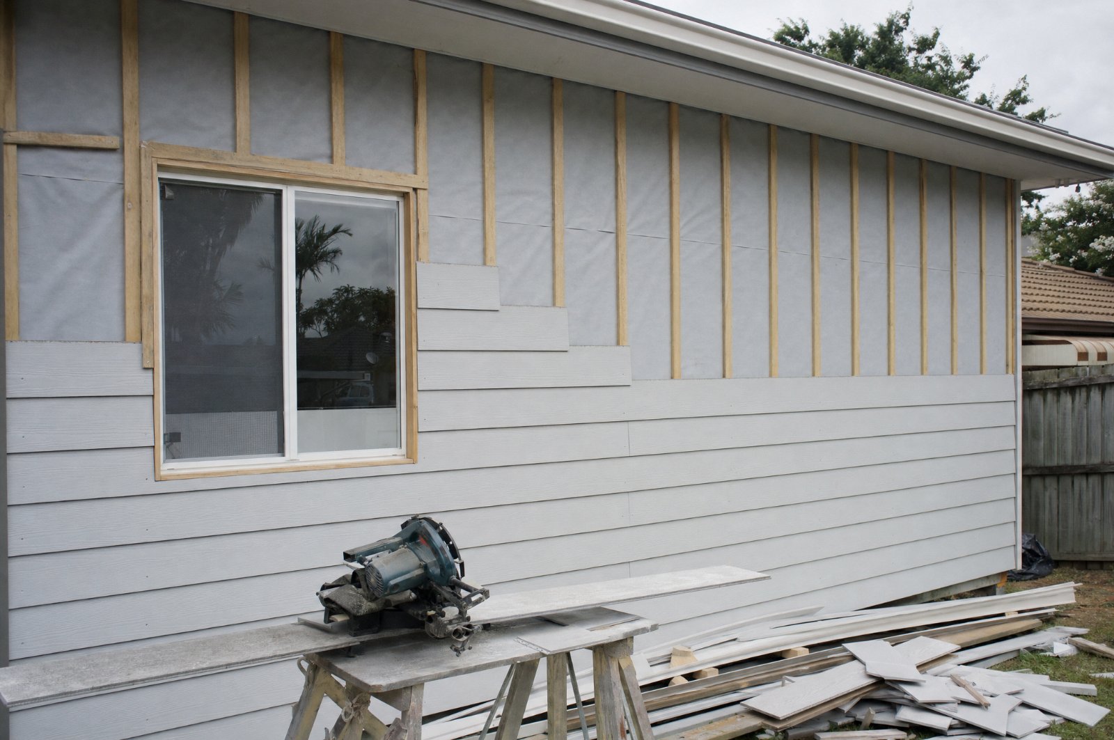 New fibre cement cladding going up in courses on a Sydney home, with timber battens over building wrap still exposed above, illustrating cladding cost Sydney factors